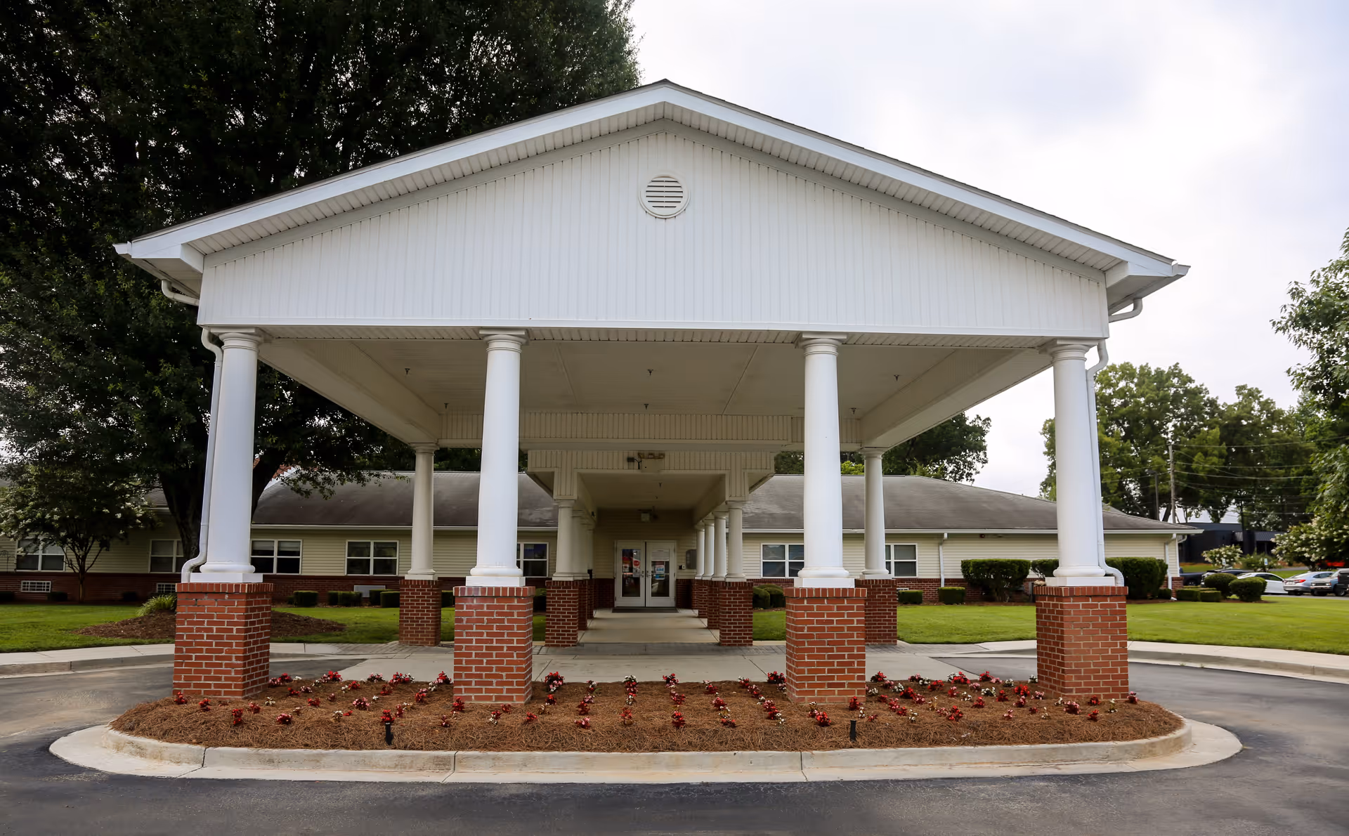 Front exterior view of Oakview Health & Rehabilitation building with a covered entrance supported by white columns on brick bases, surrounded by landscaped flower beds and green lawns.