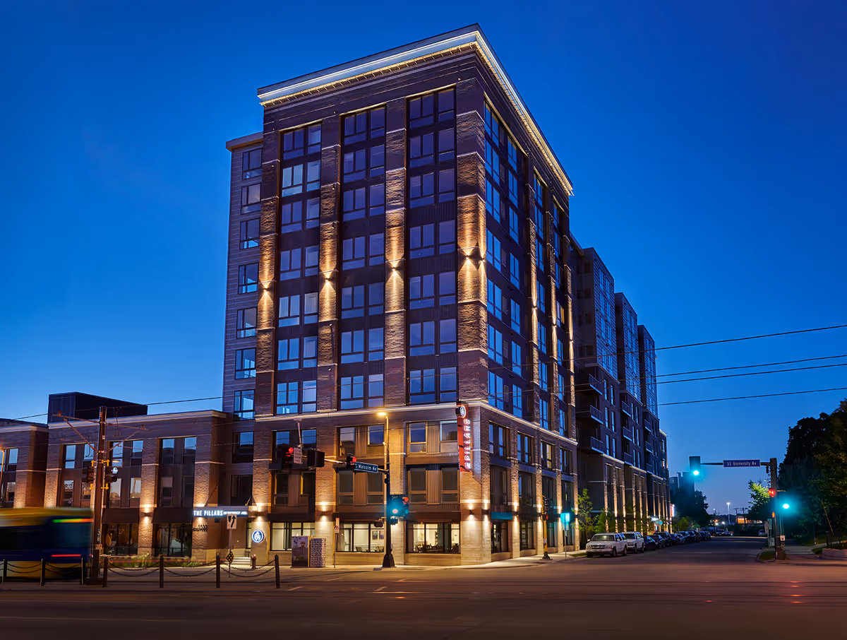 Evening street-level view of a multi-story brick building with illuminated facade and a corner entrance.