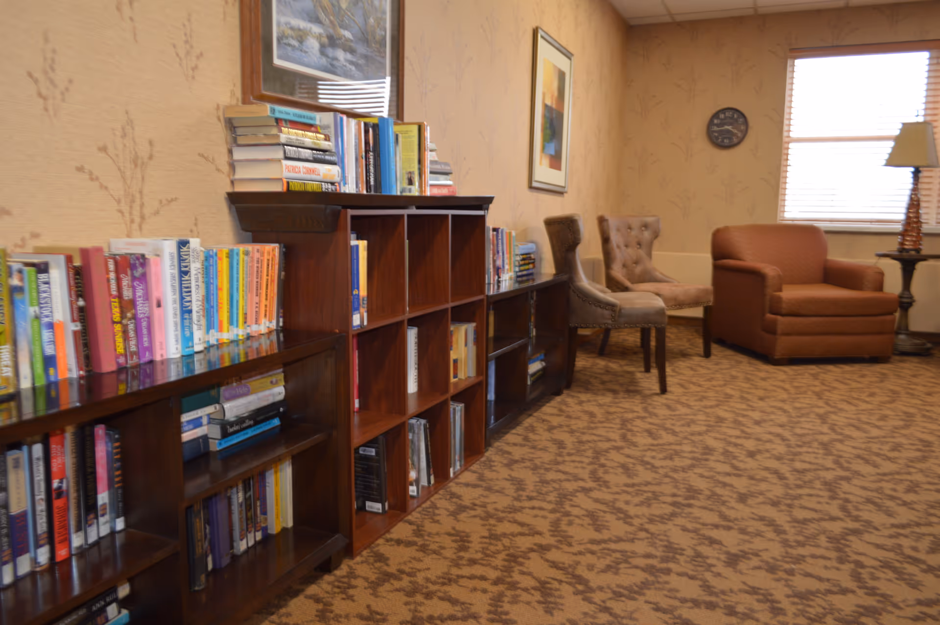 Cozy lounge area with wooden bookshelves filled with books, upholstered chairs, and a window.