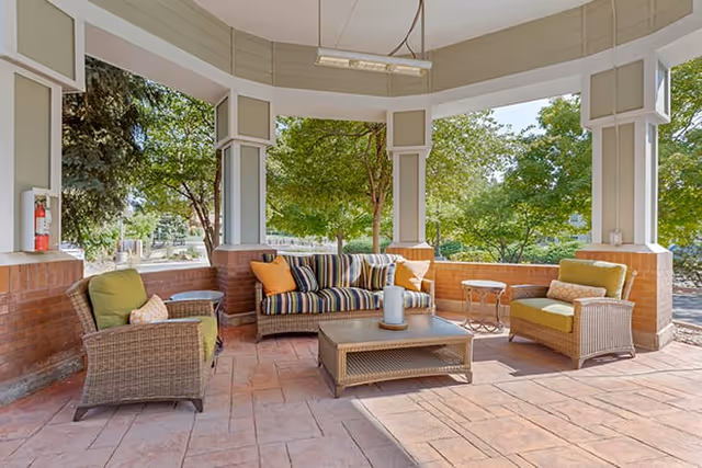 Covered outdoor patio with wicker sofa and chairs arranged around a coffee table overlooking trees.
