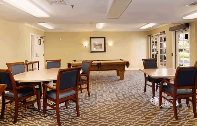 Interior common room with round and rectangular tables and chairs and a pool table in the center.