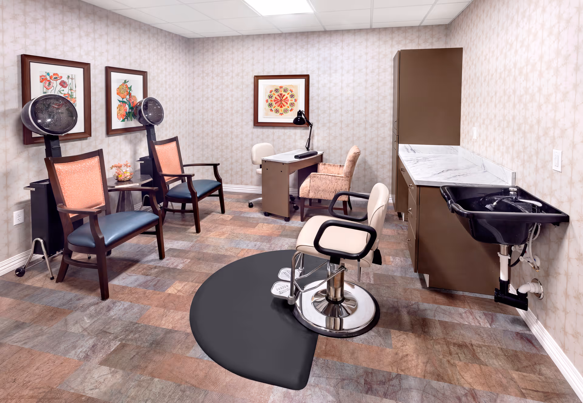 A small salon-style room with hair dryers, styling chairs, a shampoo sink, a desk, and cabinets in a senior living facility.