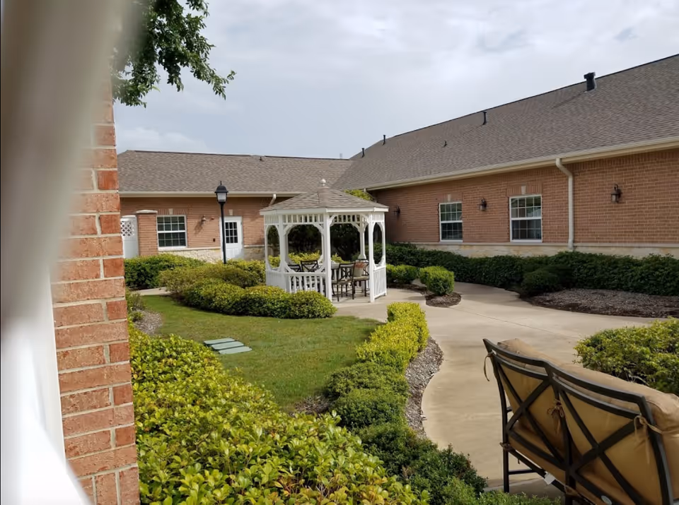 Courtyard with a white gazebo, paved walkway, benches, and surrounding brick building and landscaping.