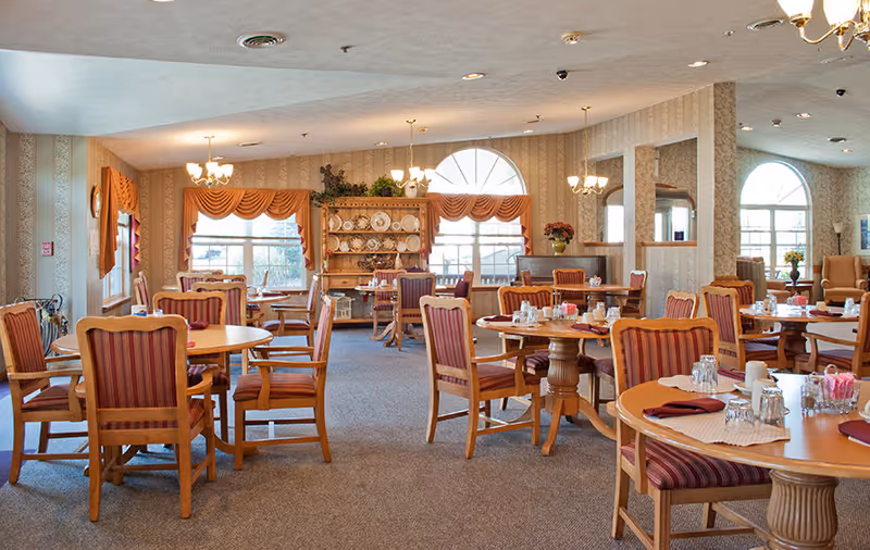 Dining room with round wooden tables, striped upholstered chairs, place settings, and warm traditional decor.