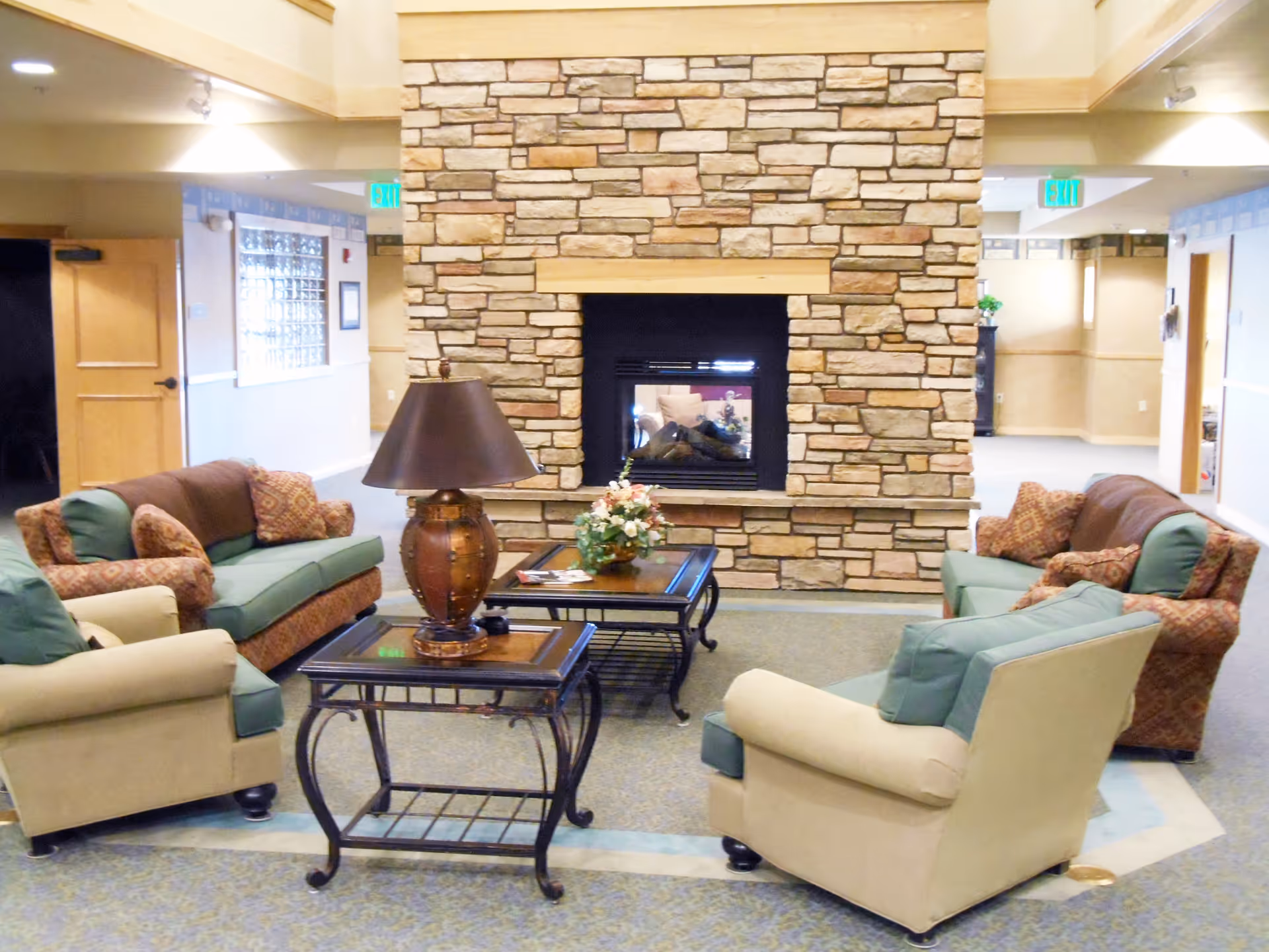Cozy communal lounge with sofas and armchairs arranged around a coffee table in front of a stone fireplace.
