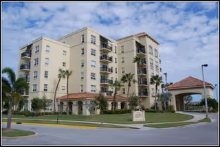 A beige multi-story senior living building with palm trees and a porte-cochère entrance.