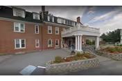 Brick senior living facility front with white porte-cochère and landscaped entrance area.