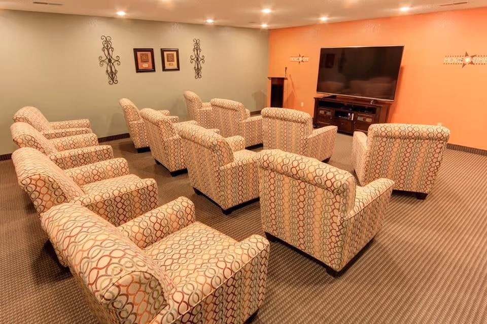 Rows of patterned armchairs arranged theater-style facing a large flat-screen TV in a cozy common room.