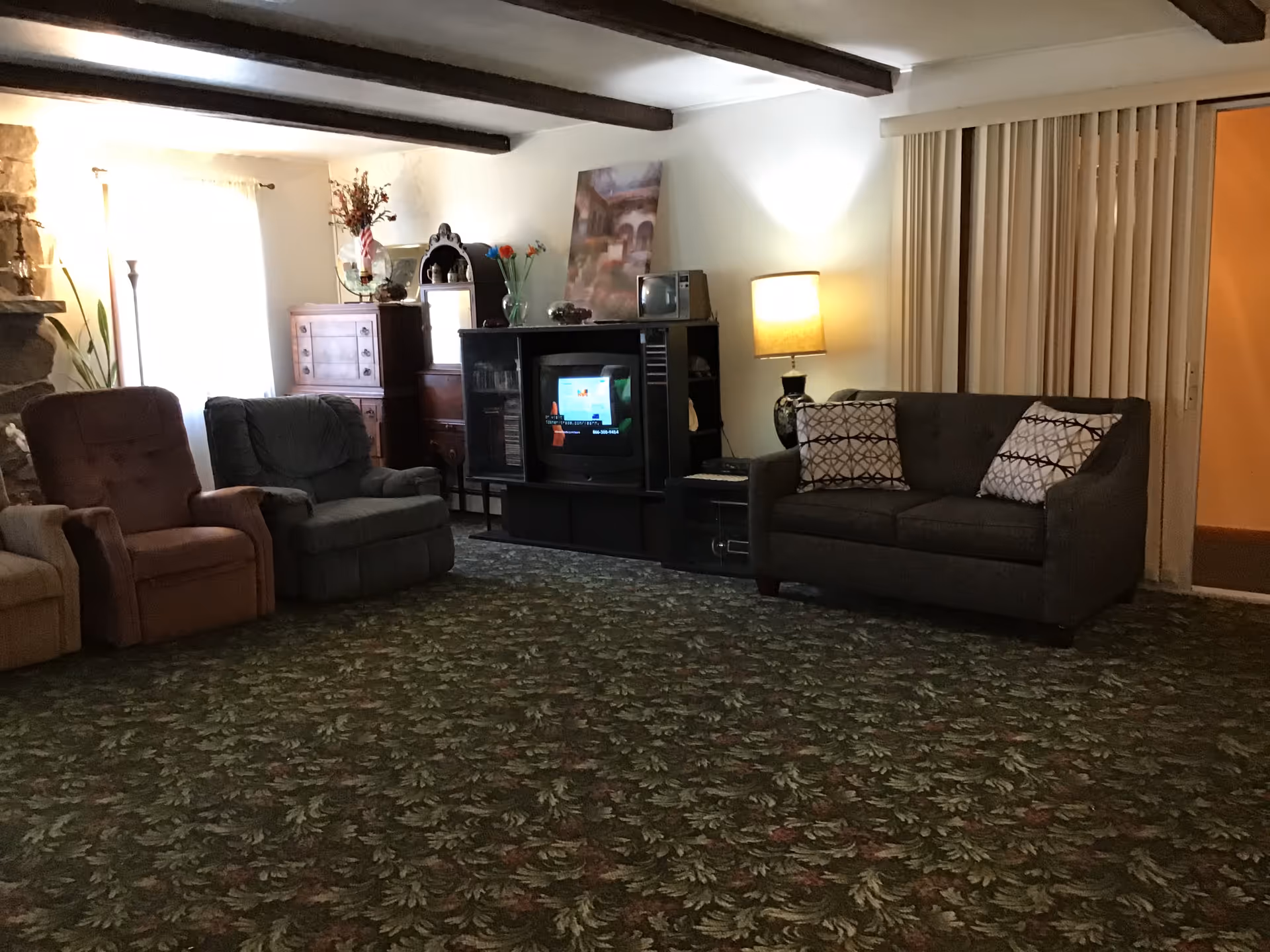 Cozy senior living room with plush chairs, sofa, TV stand, and patterned carpet.