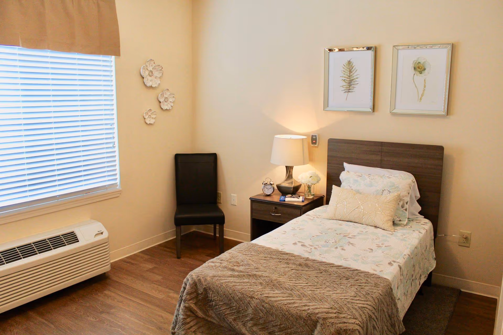 Small single bedroom with a twin bed, bedside table and lamp, a chair, and a window with blinds.
