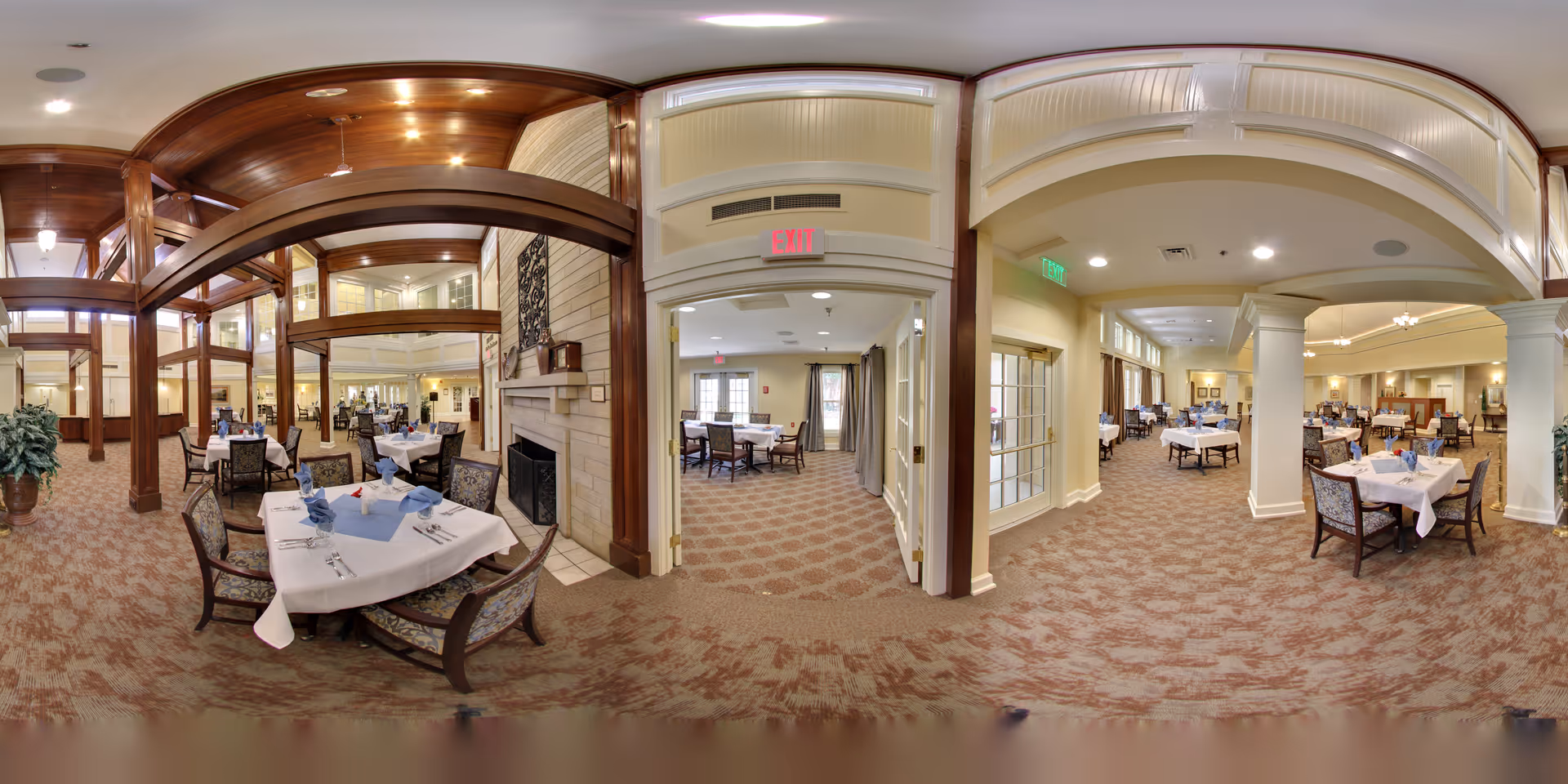 Panoramic view of a large dining room with set tables, upholstered chairs, wooden beams, and a fireplace.