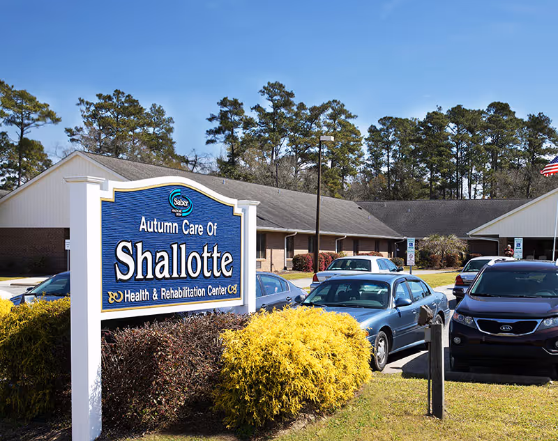 Exterior view of Autumn Care Of Shallotte Health & Rehabilitation Center with a large blue sign and parked cars in front.