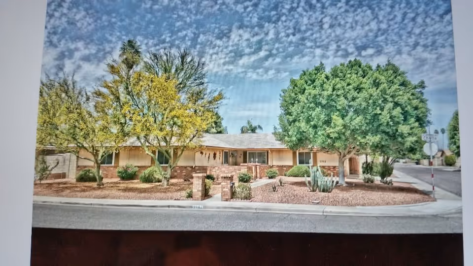 One-story beige building with desert landscaping and several trees along a curved street.