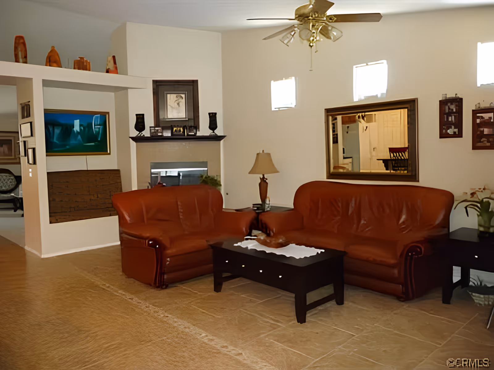 A living room with two brown leather sofas, a coffee table, a lamp, a fireplace, and a ceiling fan.