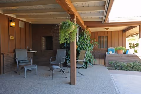 Covered outdoor seating area with several chairs, hanging plant, and brick walls.