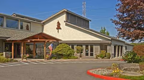 Exterior view of a senior living facility with a parking lot, landscaping, and main entrance.
