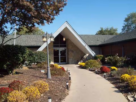A landscaped walkway leads to a glass-front entrance at a senior living center.