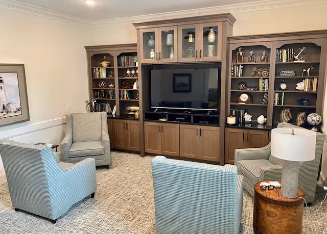 Comfortable sitting area with four upholstered armchairs arranged around a large flat-screen TV and built-in wooden shelving filled with books and decor.