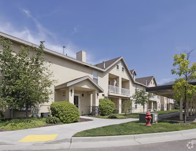 Front exterior of a two-story beige apartment building with balconies, landscaped walkways, and a red fire hydrant.
