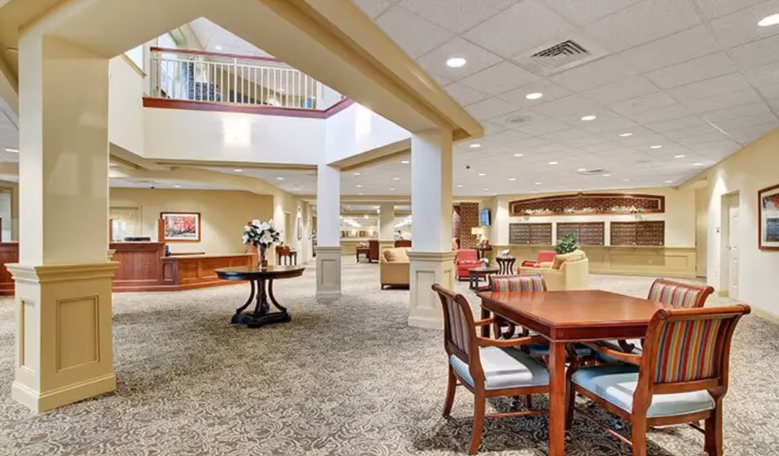 Open senior living lobby/lounge with columns, a central table with flowers, and multiple seating areas.