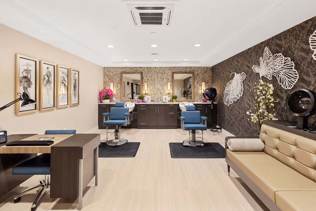 Bright salon interior with styling chairs facing mirrors, a manicure desk, and a seating area.