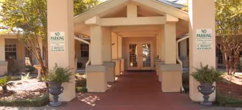 Covered walkway to Brookdale Dowlen Oaks entrance with pillars and potted plants.