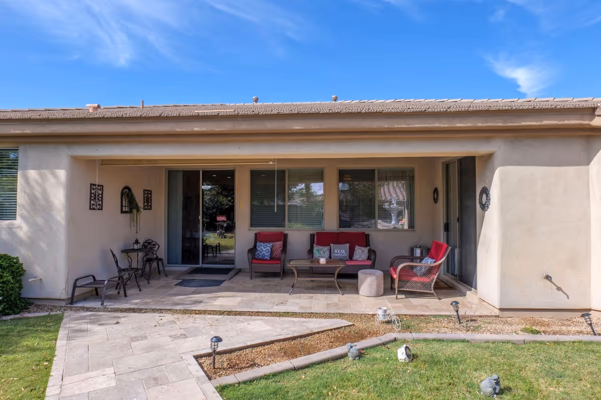 Covered backyard patio with outdoor seating, a small table, and sliding glass doors under a clear blue sky.