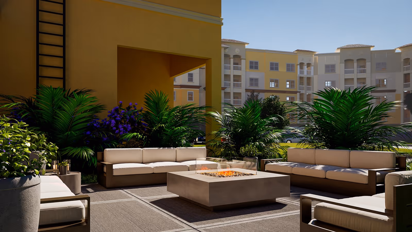 A cozy outdoor lounge area featuring comfortable seating around a modern fire pit, surrounded by lush greenery and colorful flowers, with a view of the building in the background.