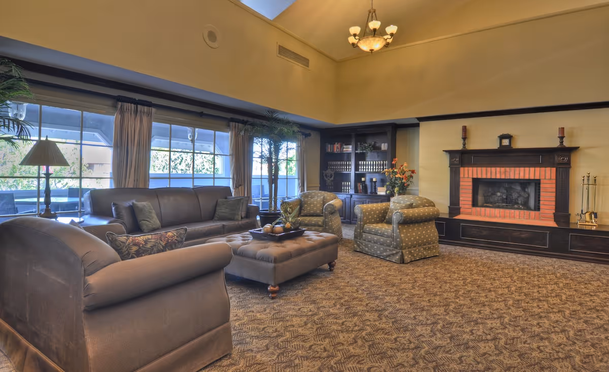 Spacious common living room with sofas, armchairs, an ottoman, large windows and a fireplace.