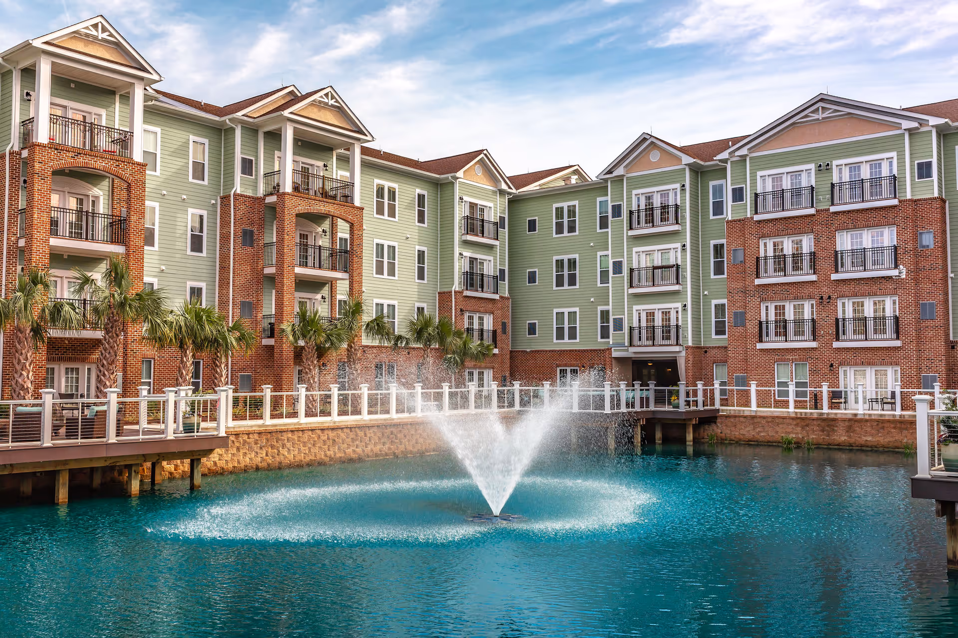 Multi-story senior living complex surrounds a central pond with a fountain and balconies.