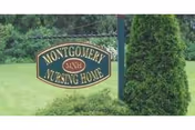 A green and gold sign reading 'Montgomery Nursing Home' mounted on a post in a grassy area with trees and bushes in the background.