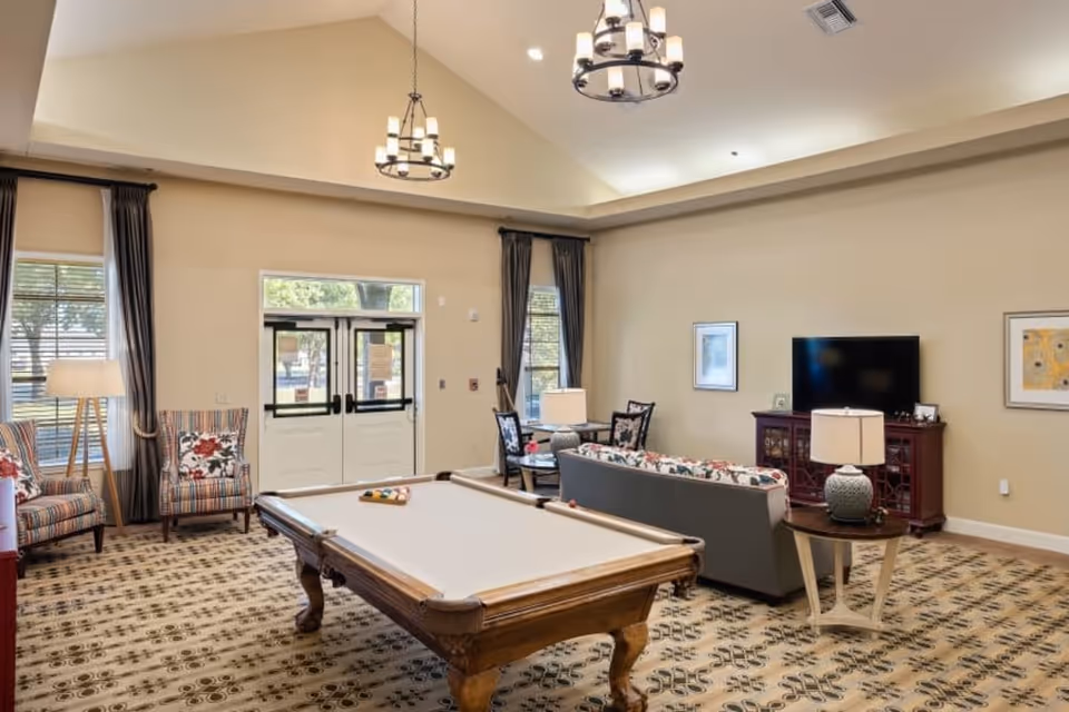 Community lounge featuring a pool table, sofa and chairs, a TV on a console, and hanging chandeliers.