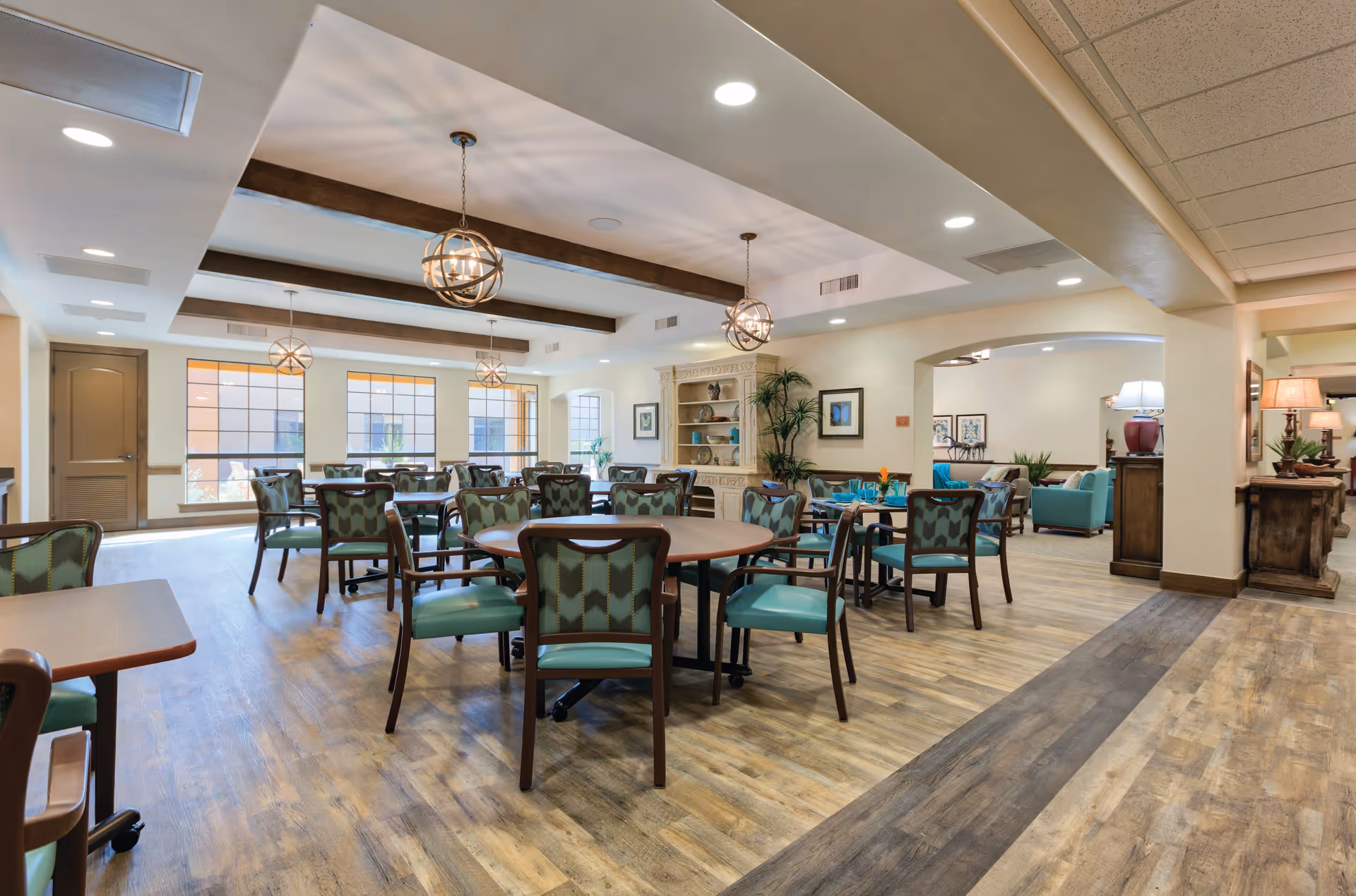 Spacious dining and common area with round tables, green-upholstered chairs, pendant lighting, and a seating nook.