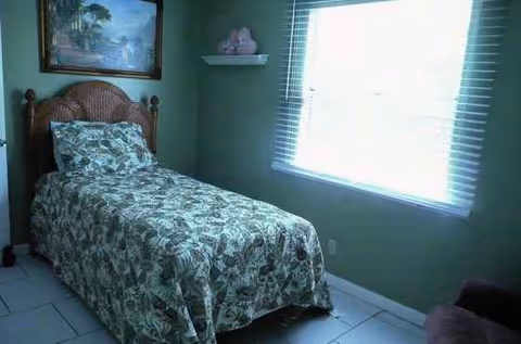 A small bedroom with a floral bedspread, wooden headboard, window, and wall art.