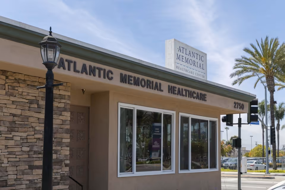 Front exterior of the Atlantic Memorial Healthcare Center building with signage above the entrance and palm trees in the background.
