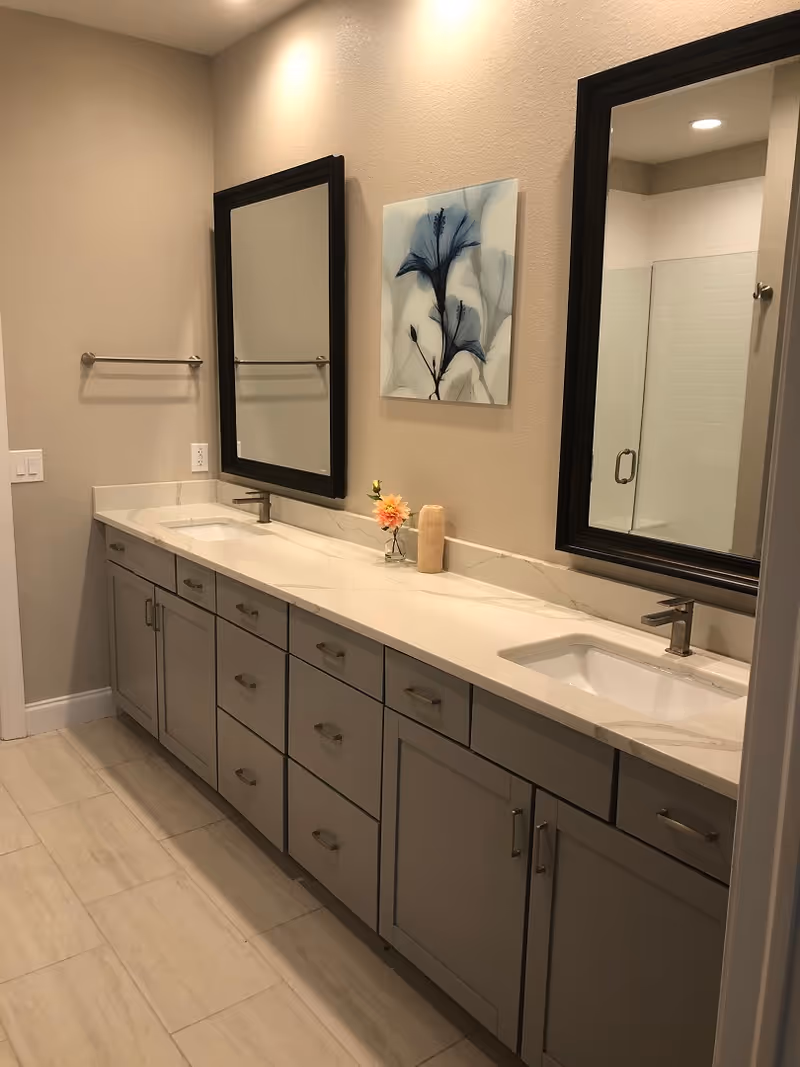 Modern bathroom with a long double-sink vanity, two mirrors, grey cabinets, and a decorative floral print on the wall.