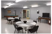 Spacious senior community common room with round tables and chairs, a pool table, and a TV against a gray wall.