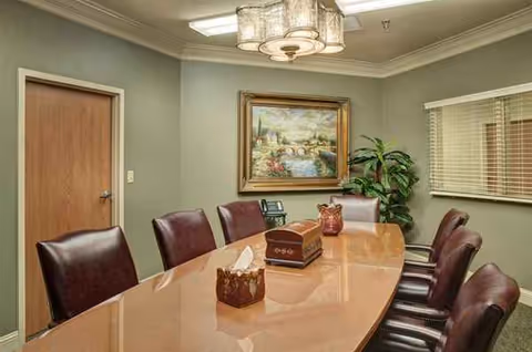 An interior conference-style room with a long wooden table, burgundy chairs, and wall art.