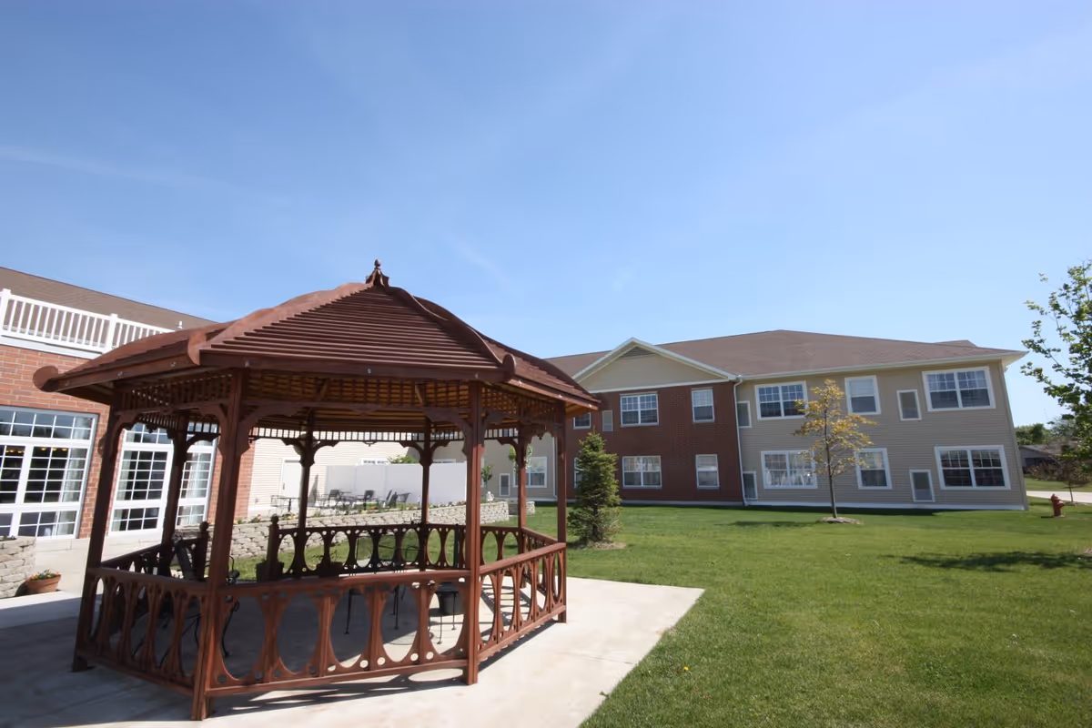 Outdoor courtyard with a wooden gazebo and the exterior of a two-story senior living building under a clear blue sky.