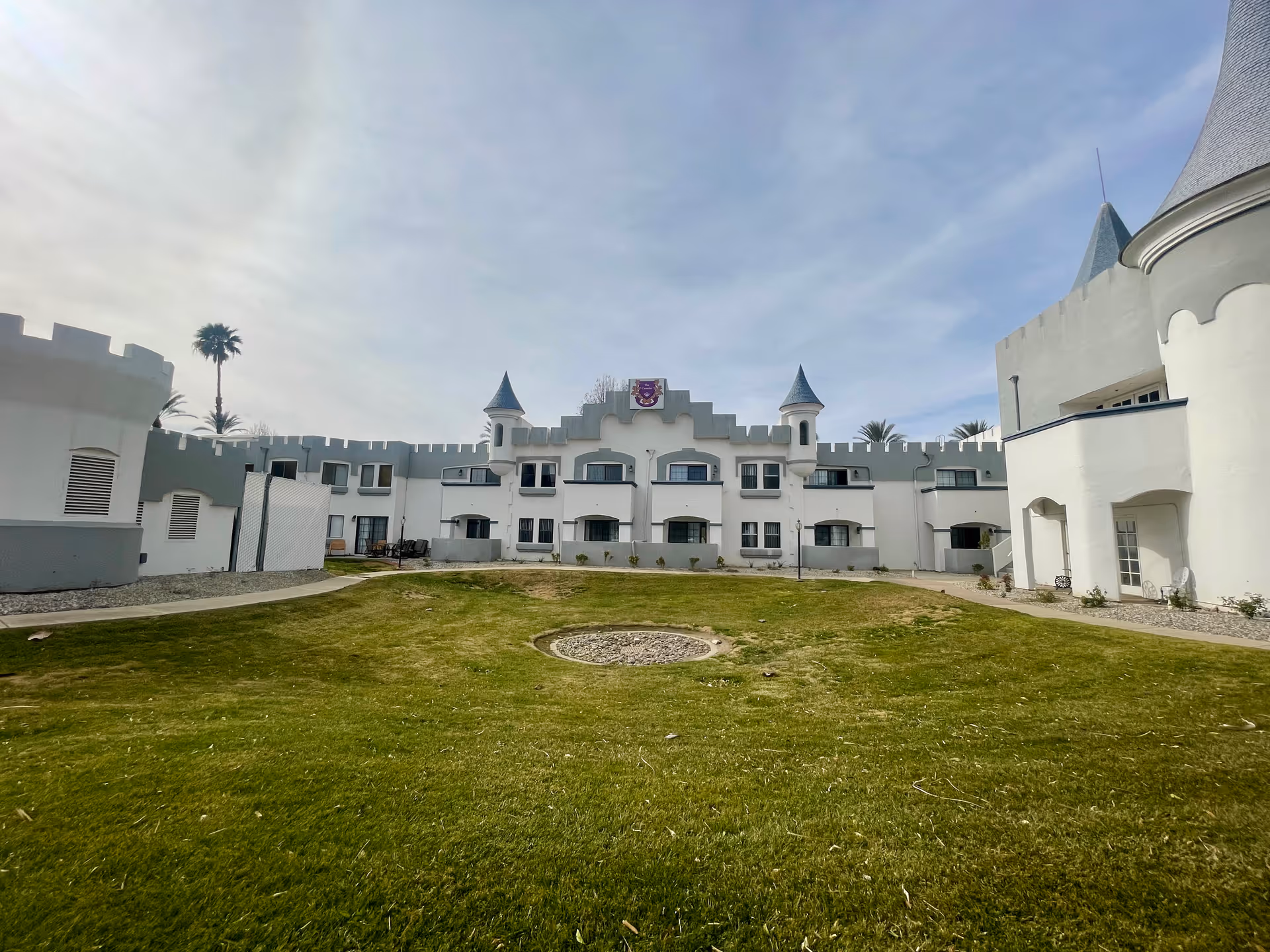 White castle-style senior living building with turrets surrounding a grassy courtyard under a cloudy sky.