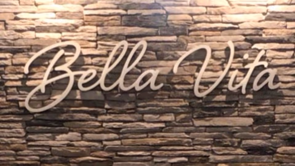 A stone wall with the words 'Bella Vita' mounted on it in large, cursive white letters.