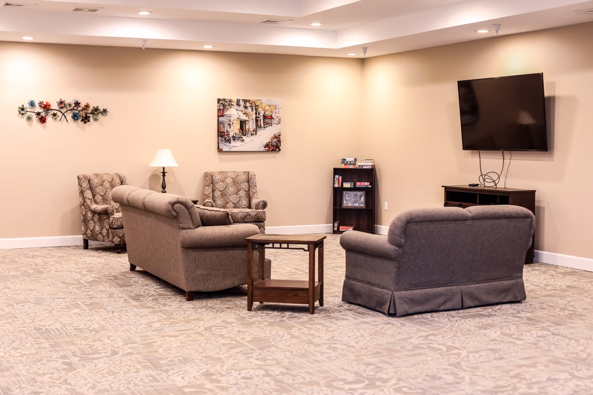 Spacious seating area with sofas, armchairs, a coffee table, wall-mounted TV, and artwork in a lounge.