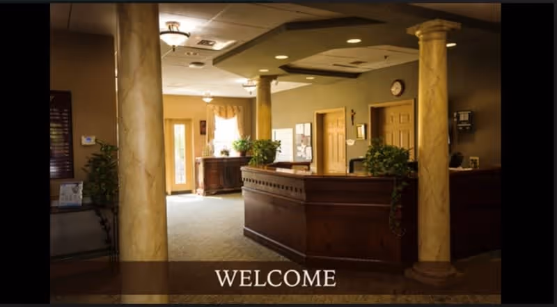 Interior view of a reception area with two large decorative columns, a wooden reception desk, plants, and a door with windows letting in natural light. The word 'WELCOME' is displayed at the bottom of the image.