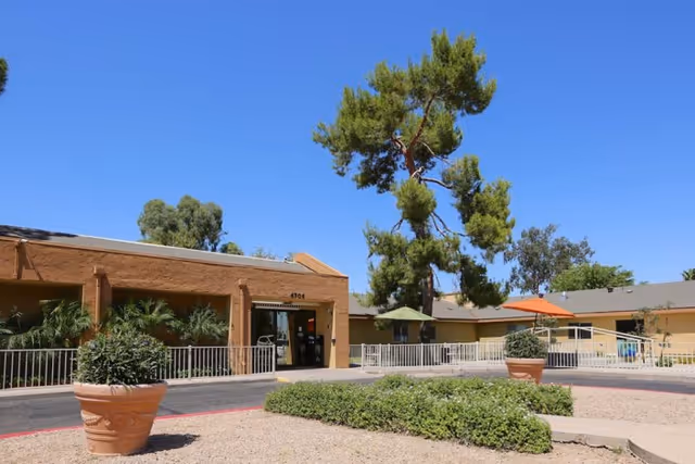 Exterior view of Horizon Post Acute And Rehabilitation Center showing a single-story building with a tan facade, surrounded by greenery including potted plants and trees under a clear blue sky.