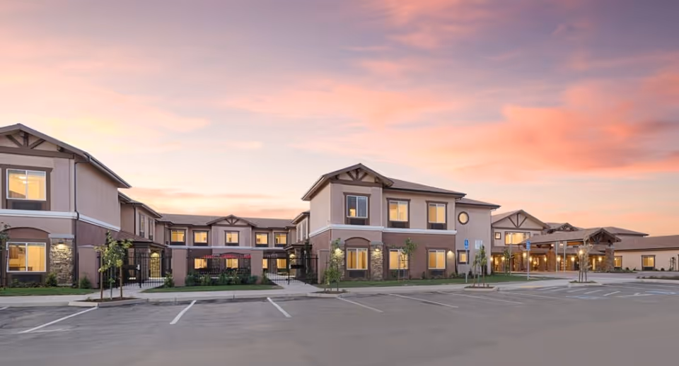 Front exterior of a two-story assisted living facility at sunset with a parking lot in the foreground.