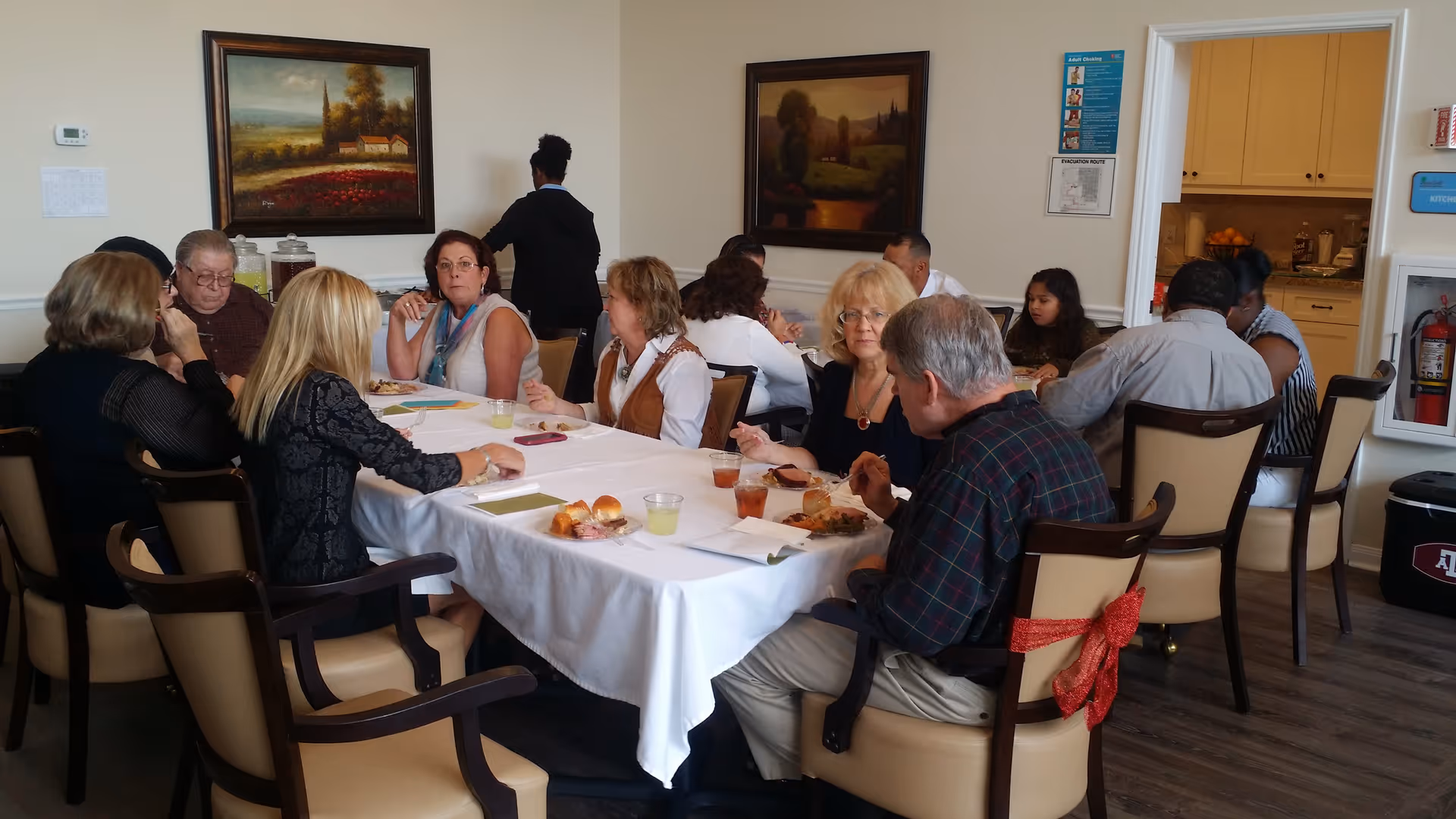 A group of people seated around a table in a communal dining room eating and talking.