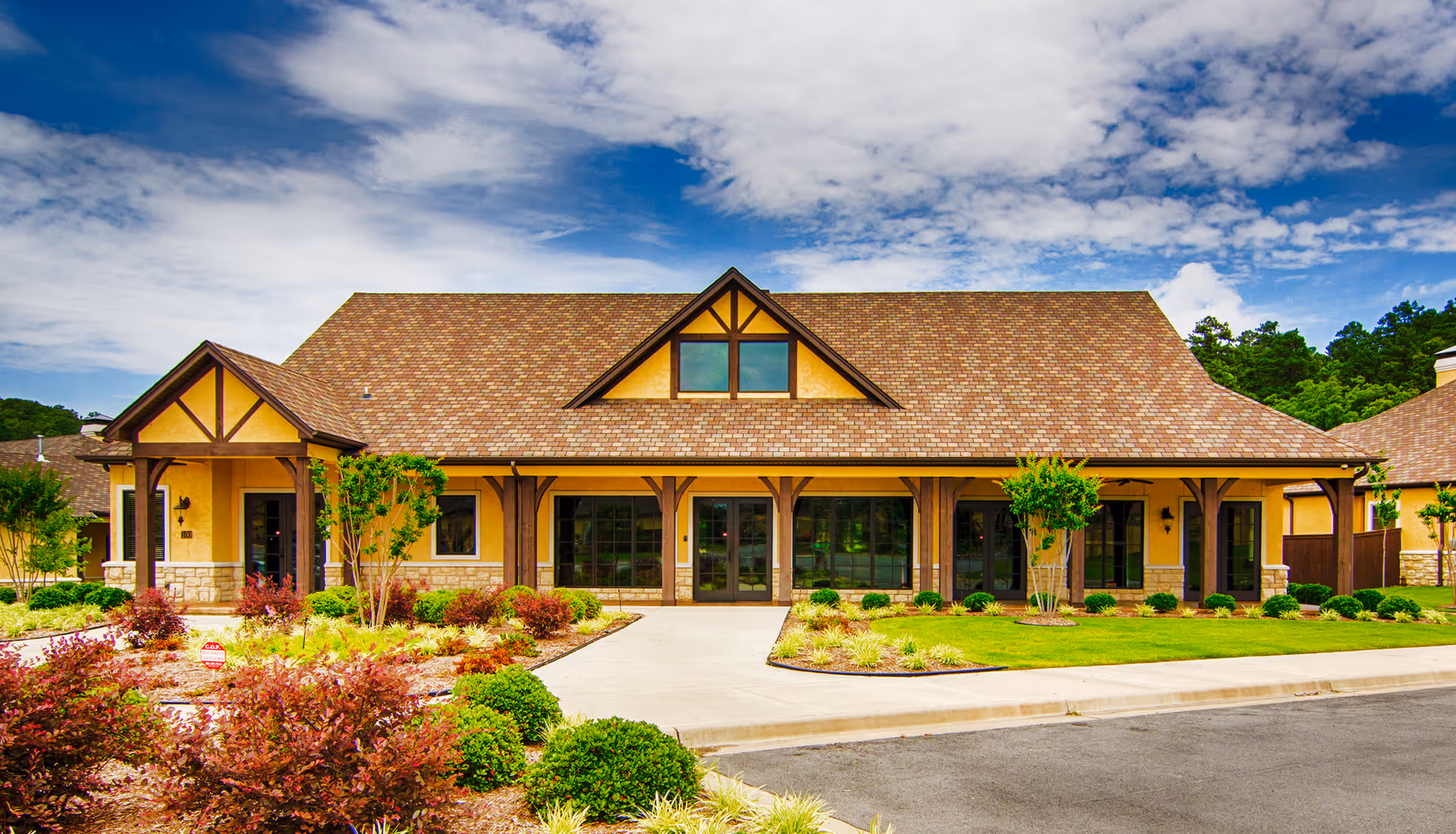 Front exterior of the Villas of Chenal building with a gabled roof, large windows, and landscaped entrance under a partly cloudy sky.