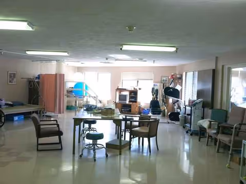 Spacious activity lounge with tables, chairs, and exercise equipment in a senior living facility.