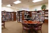 Well-lit community library with bookshelves along the walls and a round table with chairs in the center.