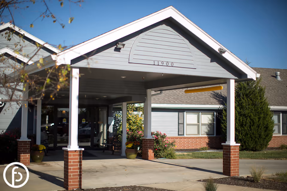 Covered front entrance and drive-through portico of a senior living building with brick pillars and the address "11900" above the entry.